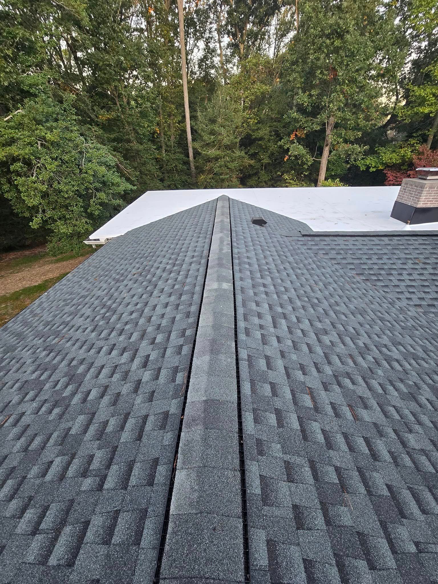 A close up of a roof with a chimney and trees in the background.