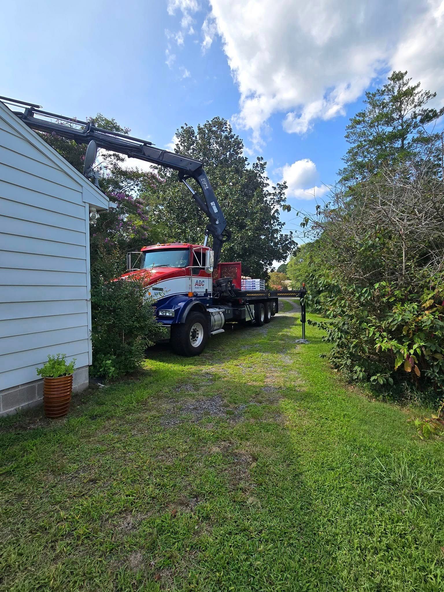 A red , white and blue truck with a crane on the back is parked in front of a house.