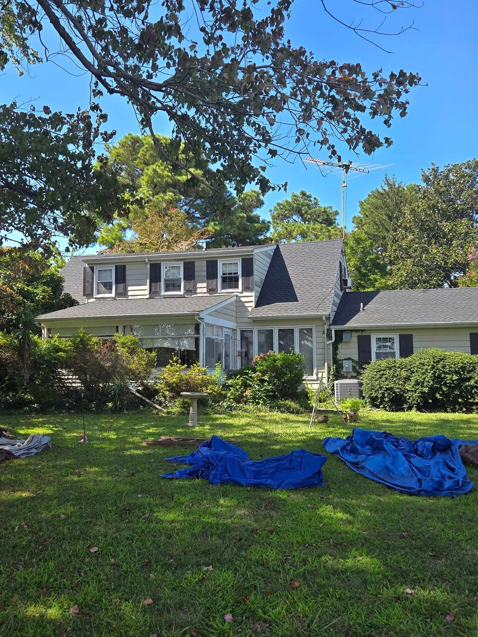 A house with a blue tarp on the grass in front of it.