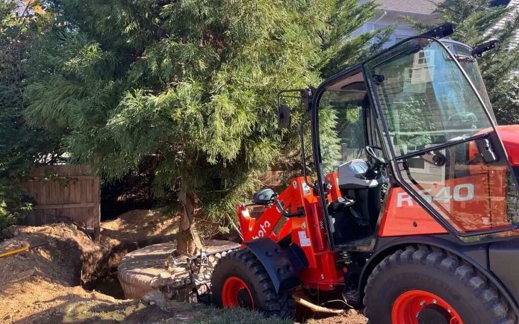 Red wheel loader digging in a yard near trees.