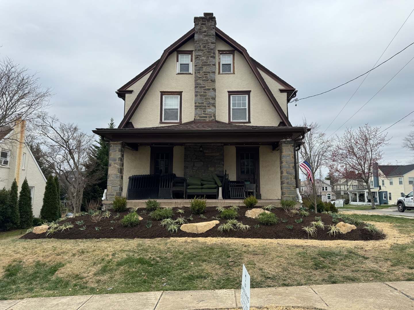 Two-story house with stone chimney and porch, new landscaping in front. Cloudy sky.