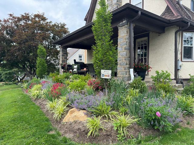 Colorful flower garden in front of a house with a stone porch.