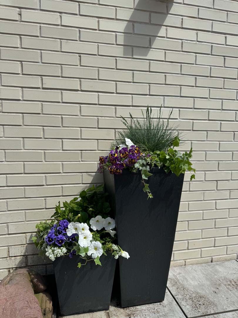 Two black rectangular planters with colorful flowers against a beige brick wall.
