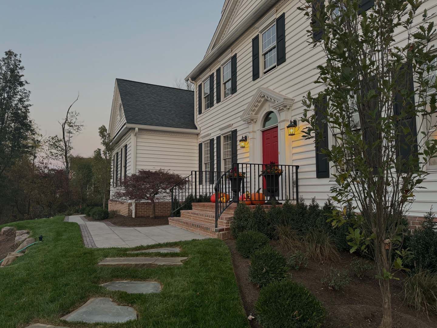 White house with black shutters and red door; pumpkins on porch.