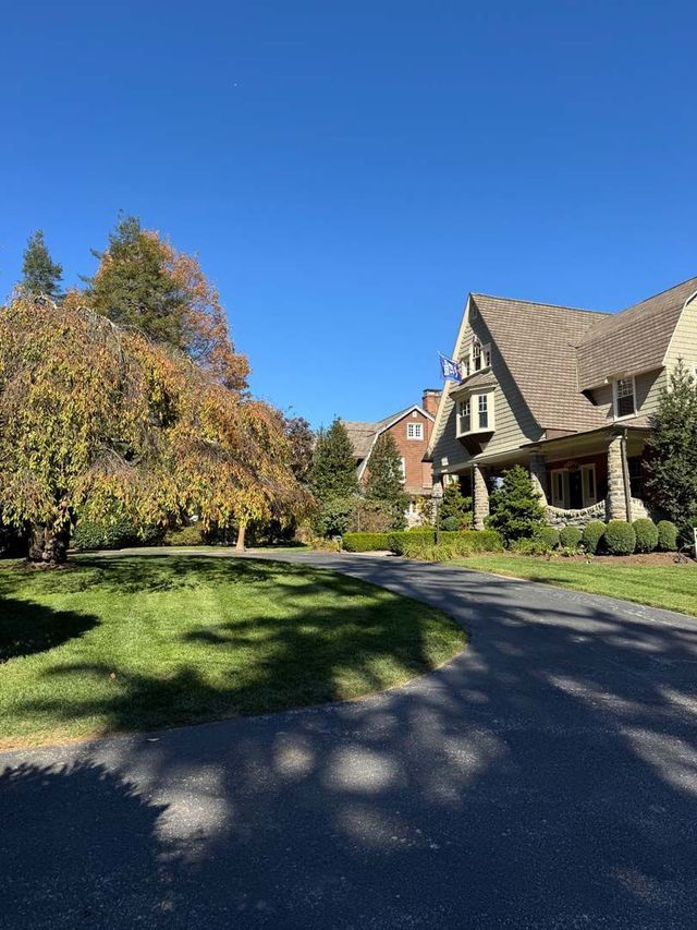 Houses on a tree-lined street with sunny sky. Brown roofed homes, green trees and lawn.