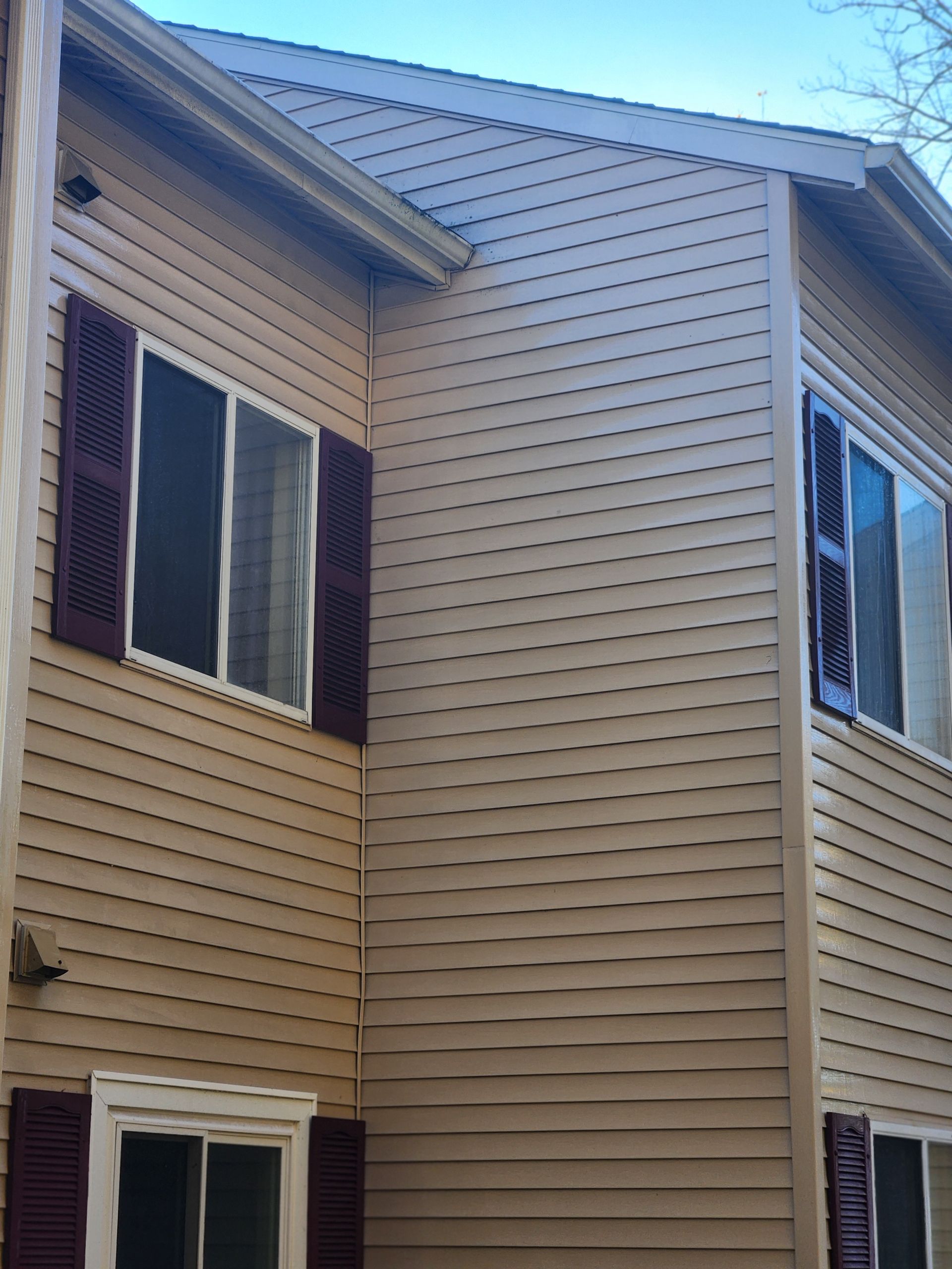 A house with a tan siding and red shutters on the windows.