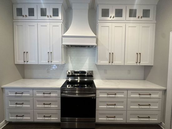 Bright white kitchen with central stainless steel stove, hood, and cabinets on both sides