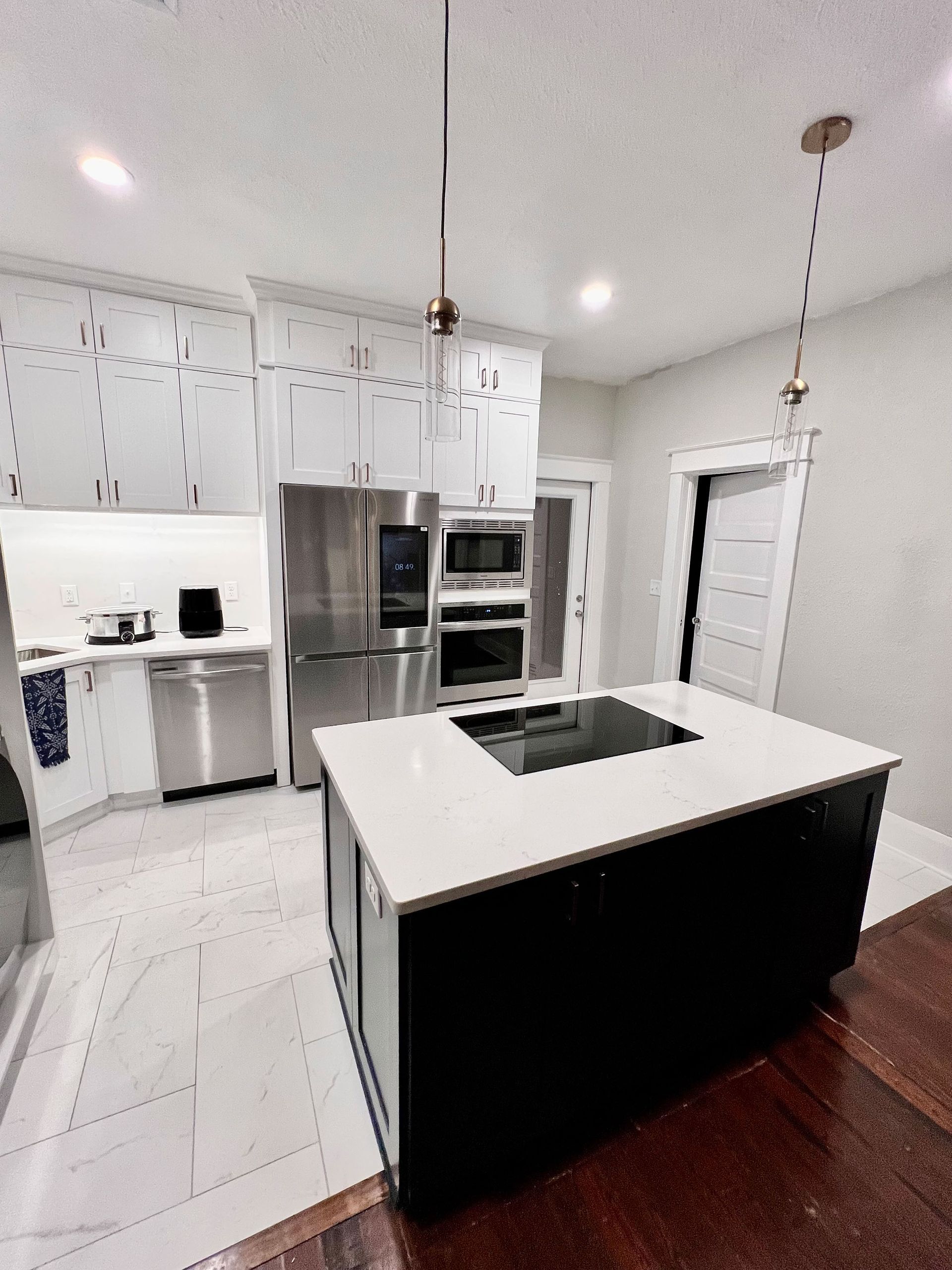 Modern white kitchen with stainless steel appliances, black island, and pendant lights
