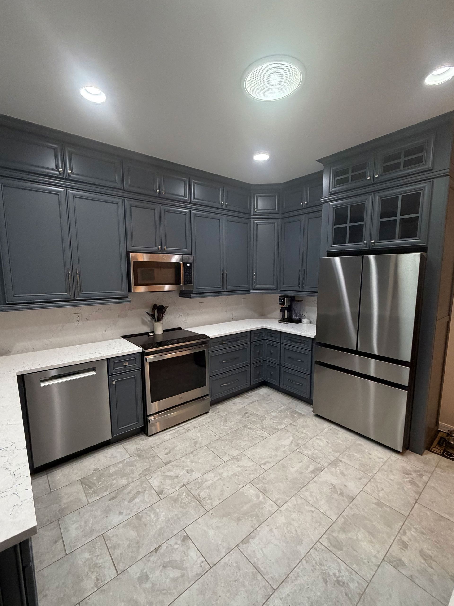 Modern gray kitchen with stainless steel appliances, white countertop, and tiled floor