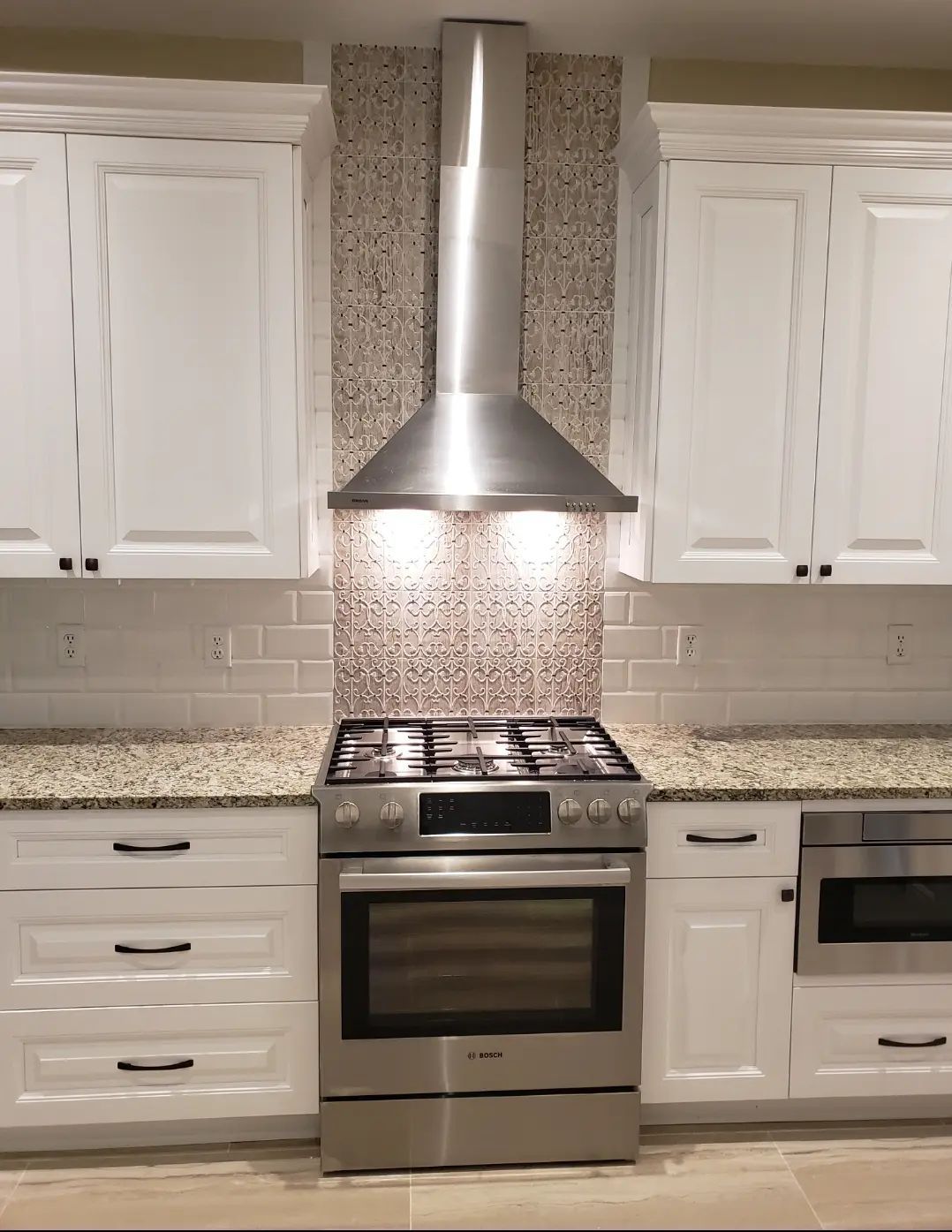 Modern kitchen with white cabinets, granite countertops, stainless steel stove, and range hood