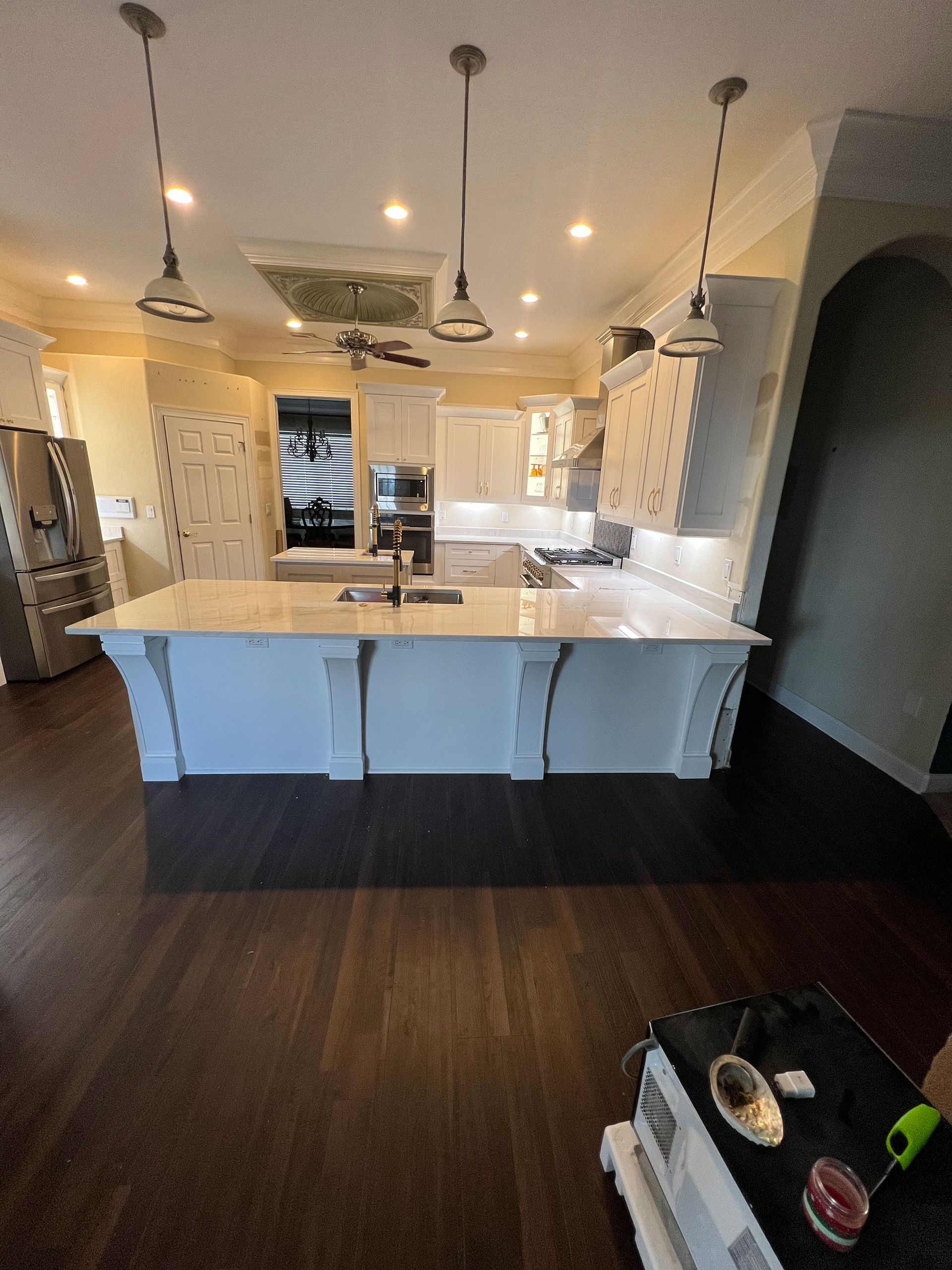 Modern kitchen with white island, pendant lights, dark wood floors, and stainless appliances