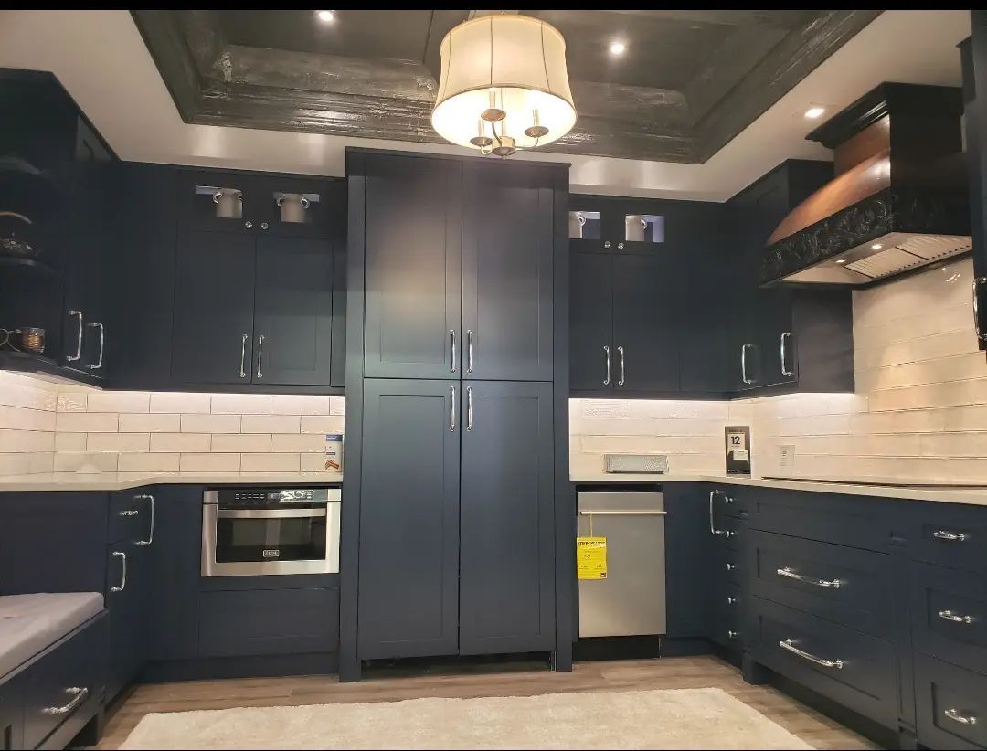 Modern kitchen with dark cabinets, white subway tile backsplash, and a central stainless-steel refrigerator.