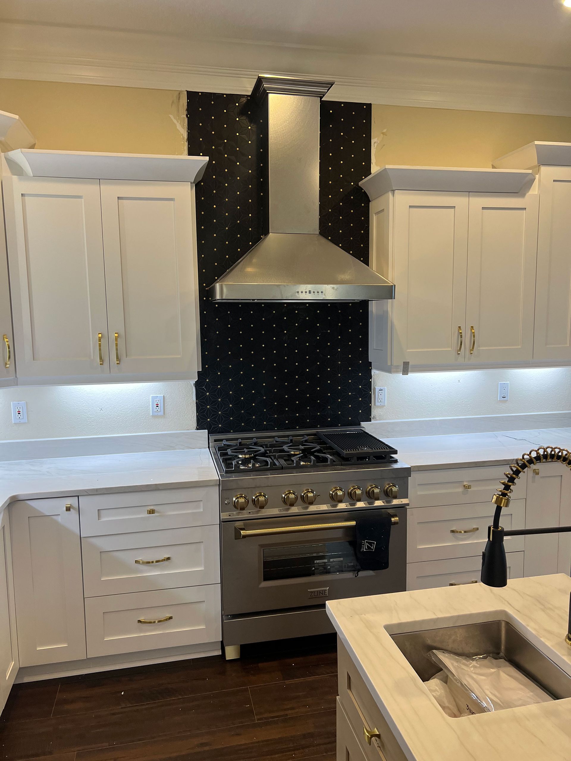 White kitchen with black backsplash, stainless range hood, built-in cabinets, and a farmhouse sink.