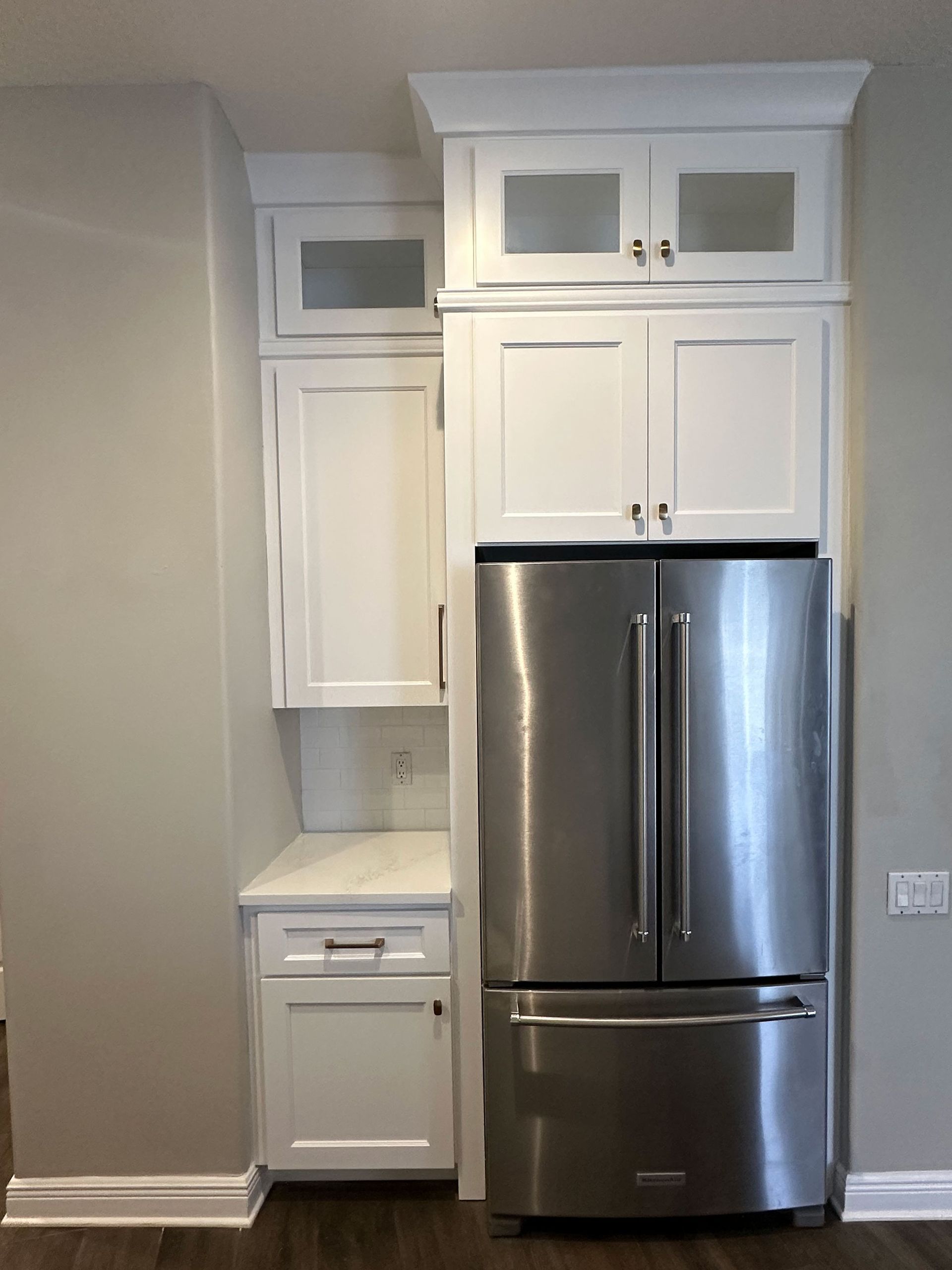 Small kitchen nook with stainless steel refrigerator, white cabinets, and a beige wall.