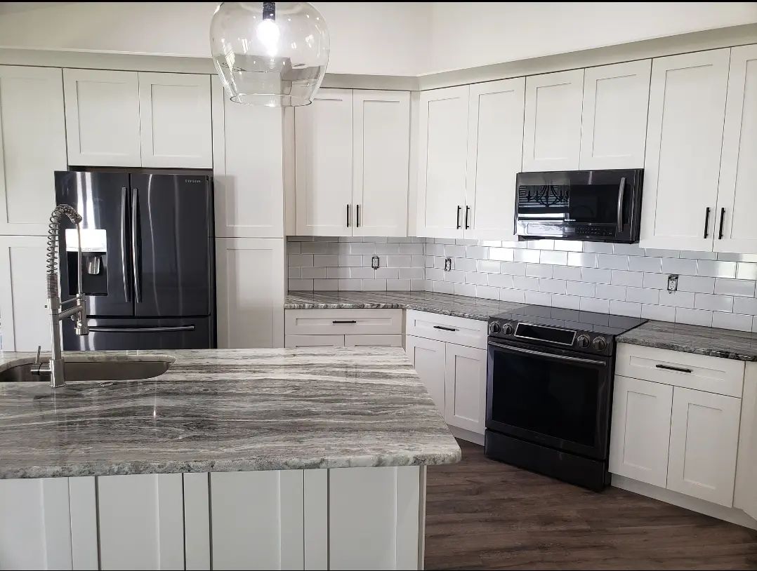 Bright white kitchen with black appliances, granite island, and wood flooring