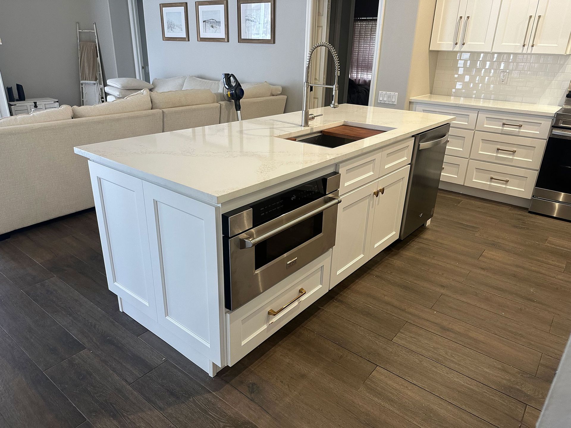 Modern kitchen with white island, built-in oven, sink, and dark wood flooring.