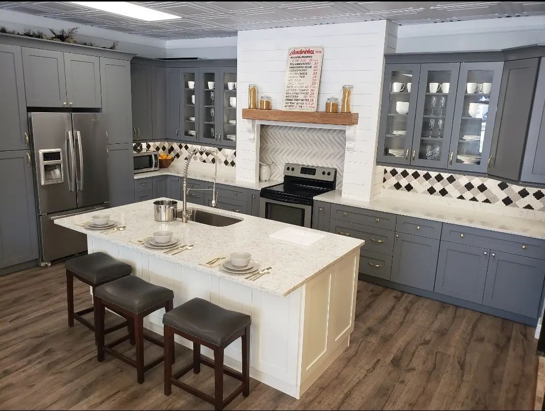 Modern gray kitchen with island, three stools, stainless fridge, and white range hood over stove.