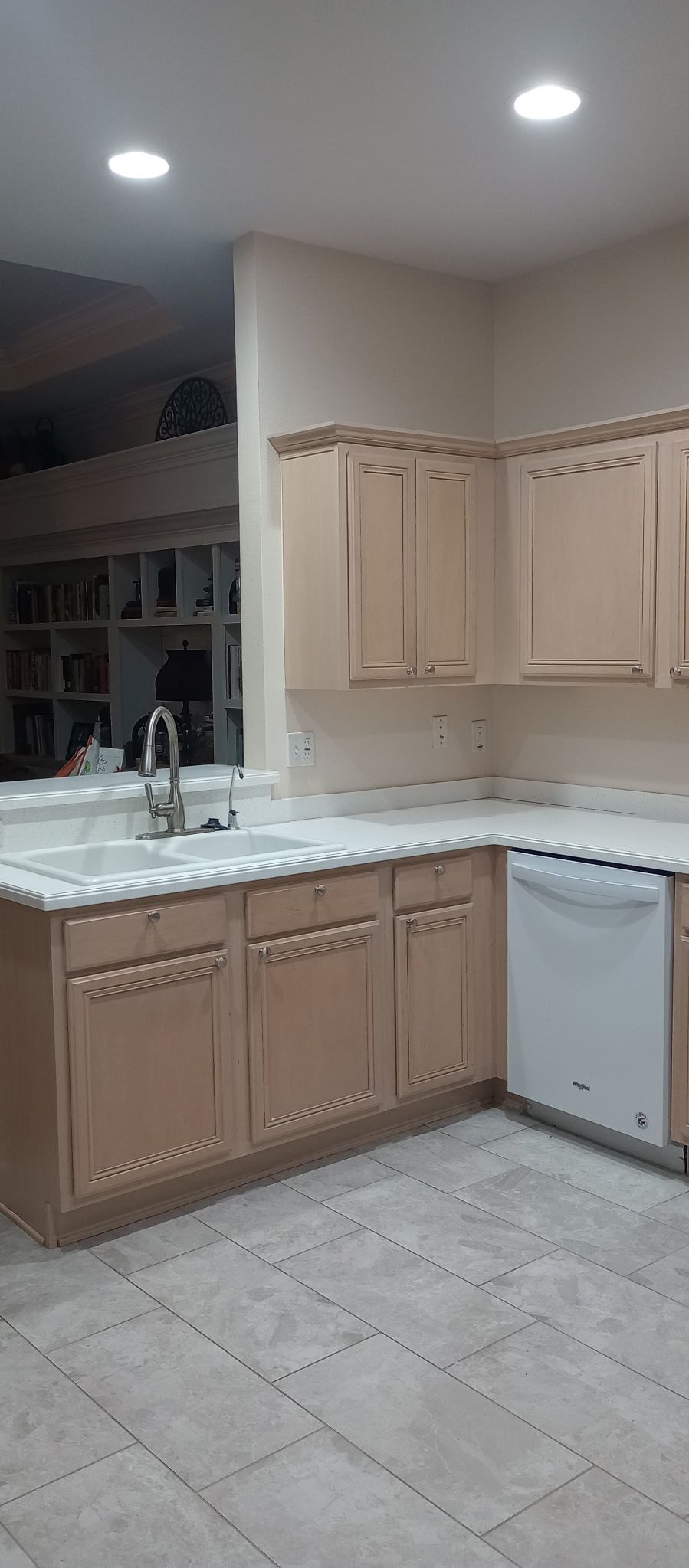 Small beige kitchen with wooden cabinets, white countertops, tiled floor, sink, and dishwasher under recessed lights