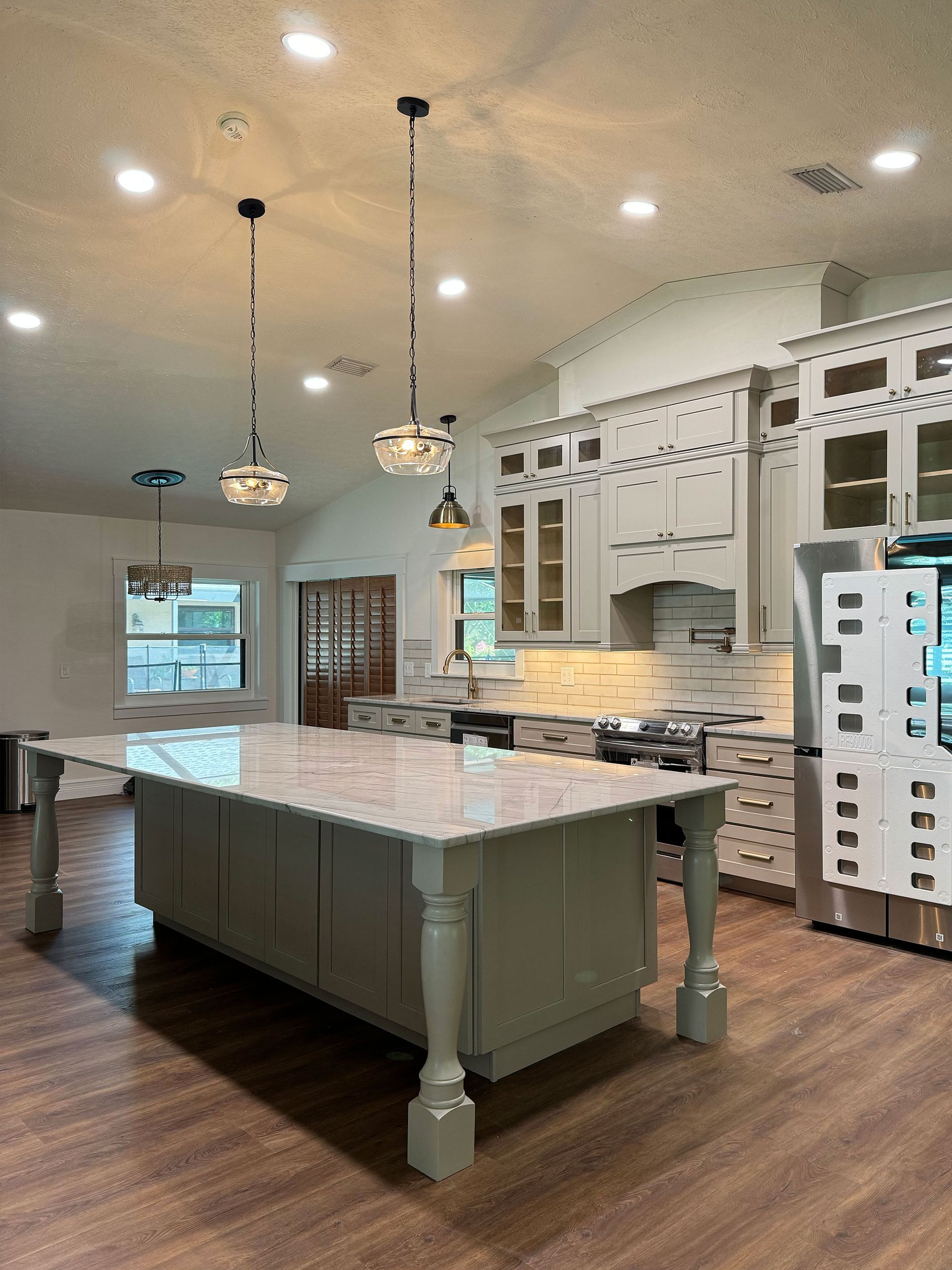 Spacious kitchen with a large island, white cabinets, pendant lights, and dark wood floors.