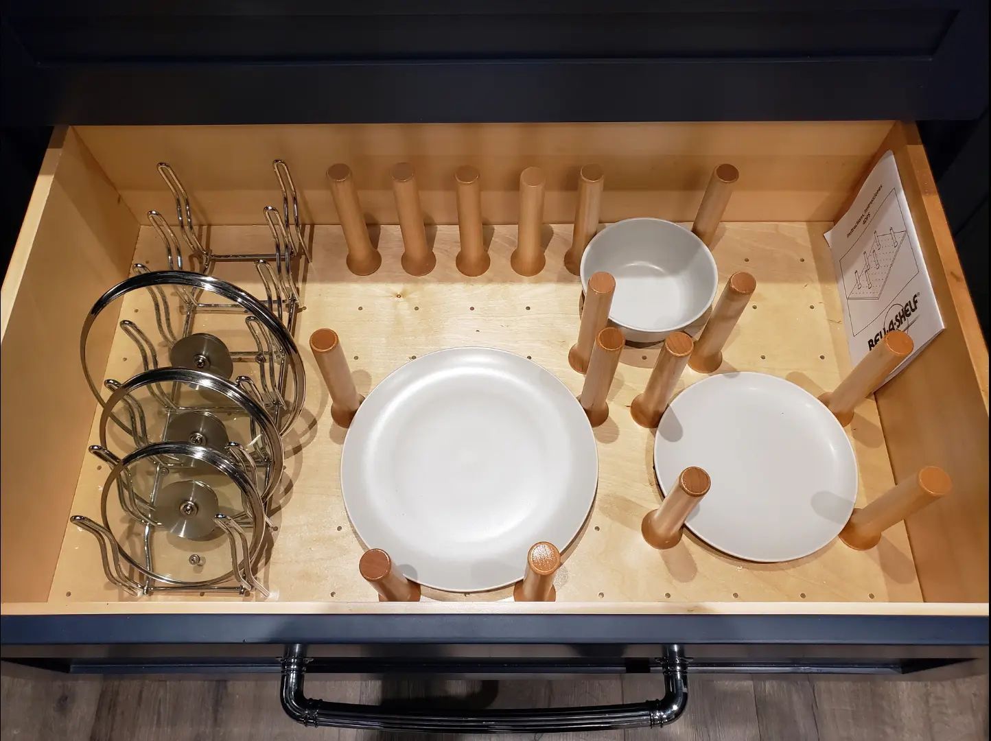 Open drawer with organized kitchen items: plates, bowls, mugs, and small wooden pegs.
