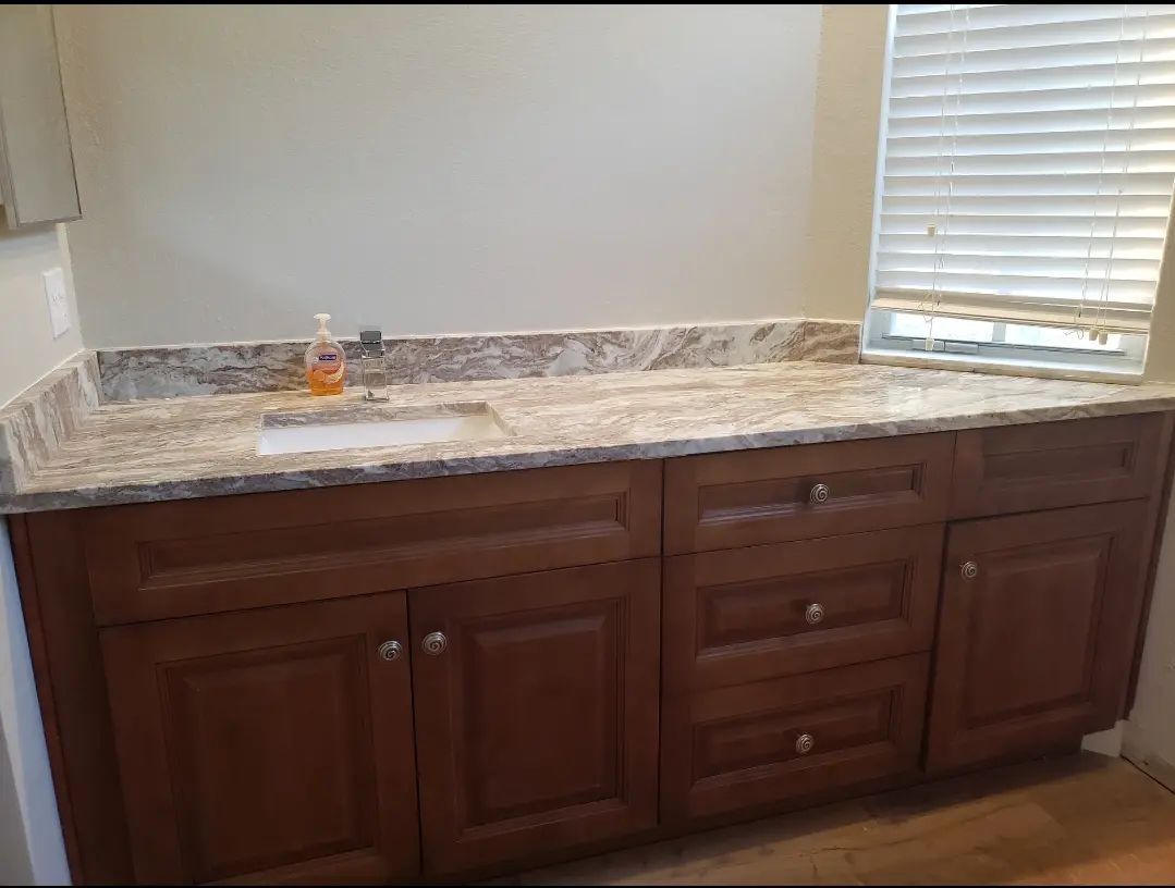 Bathroom vanity with dark wood cabinets and marble countertop beneath a window with blinds