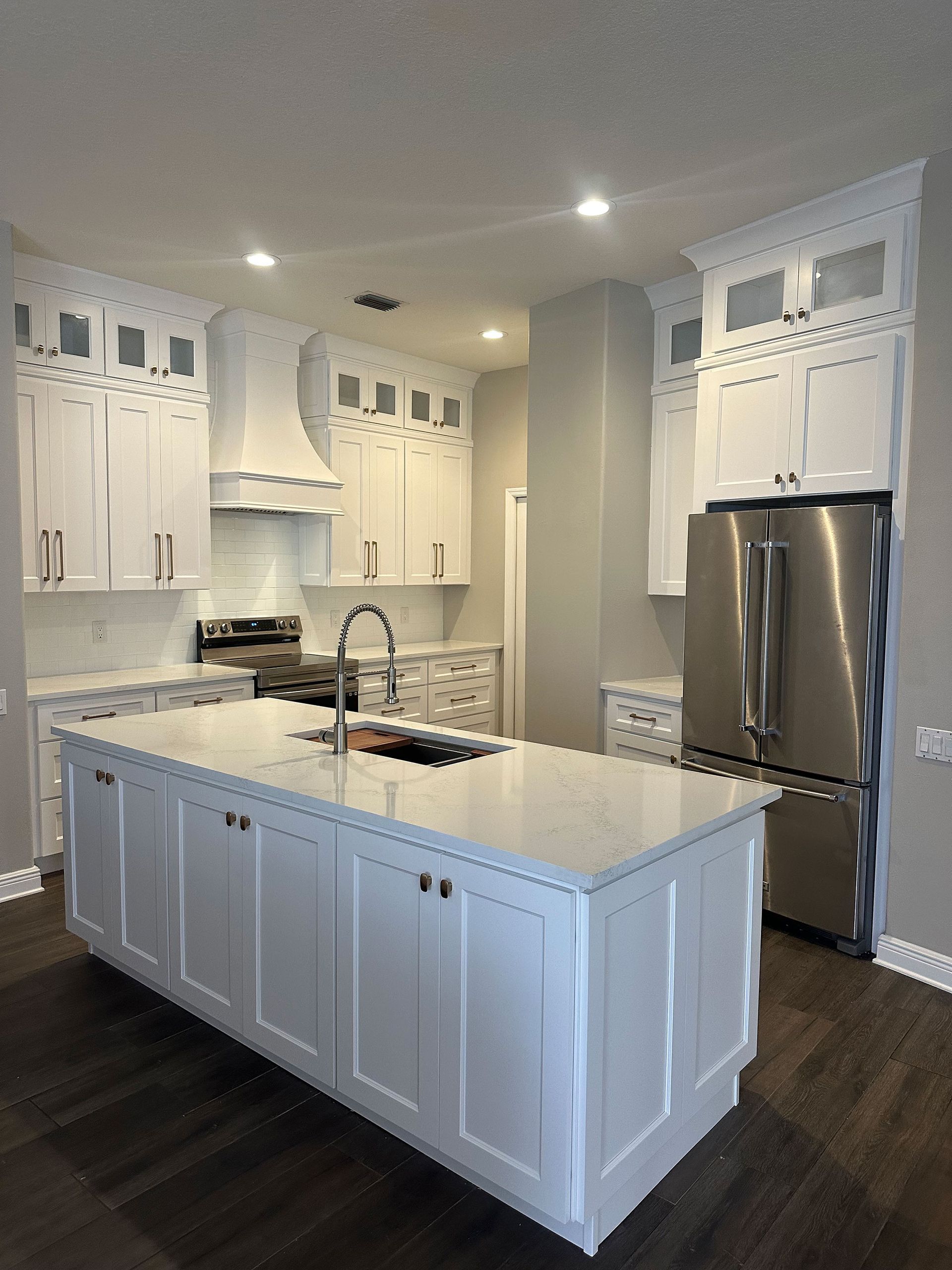 Modern white kitchen with a large island, stainless steel fridge, and dark hardwood floors