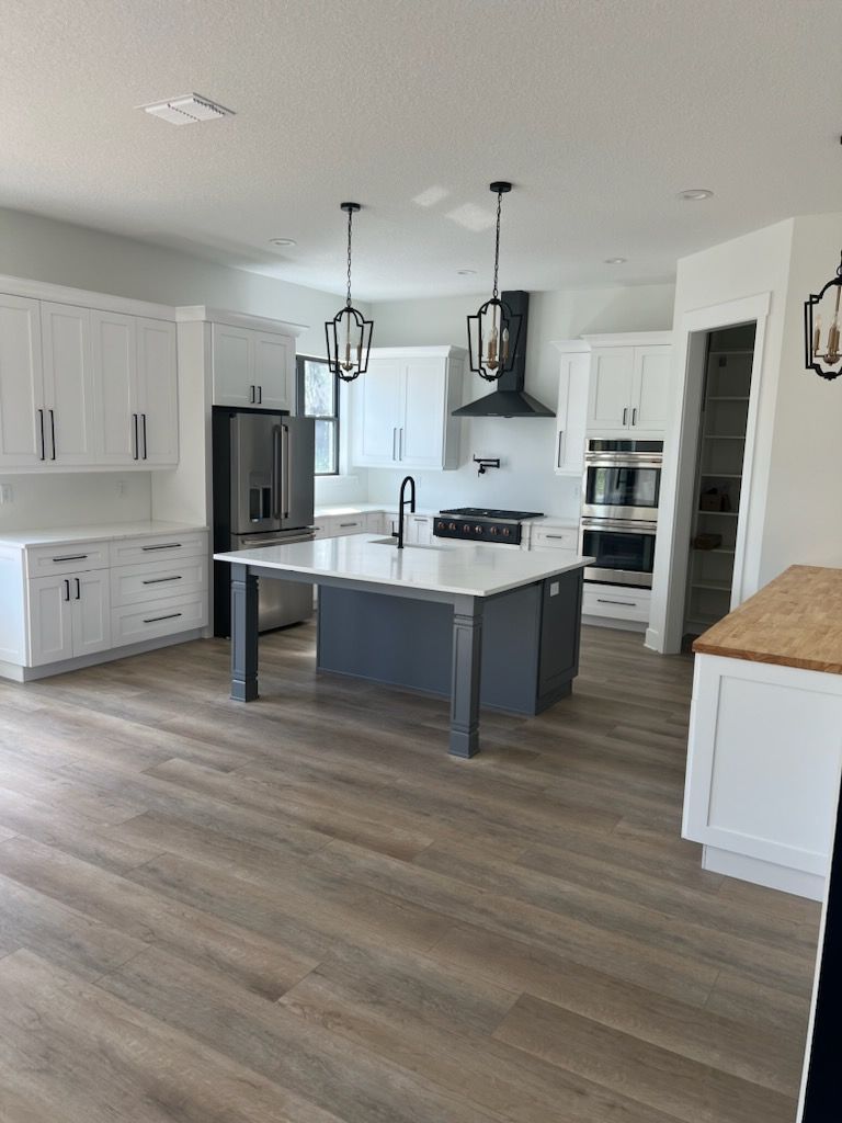 Modern white kitchen with gray island, stainless appliances, pendant lights, and wood-look flooring