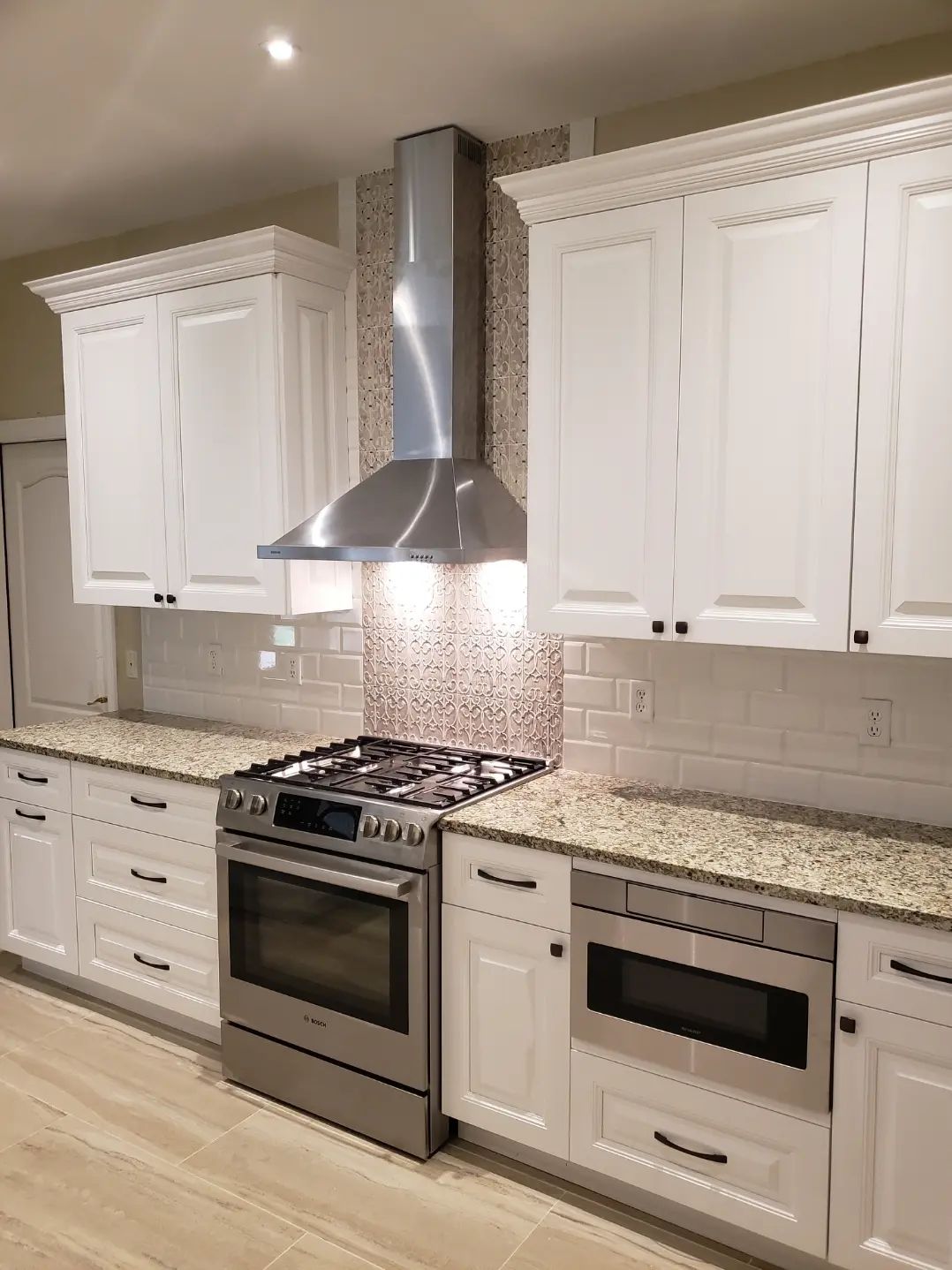 Modern white kitchen with stainless steel range hood, stove, and built-in microwave drawer