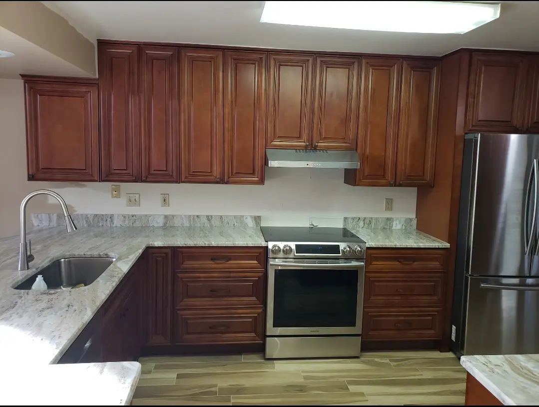 Dark wood kitchen cabinets, granite countertop, stainless stove and fridge, with a sink on the left.