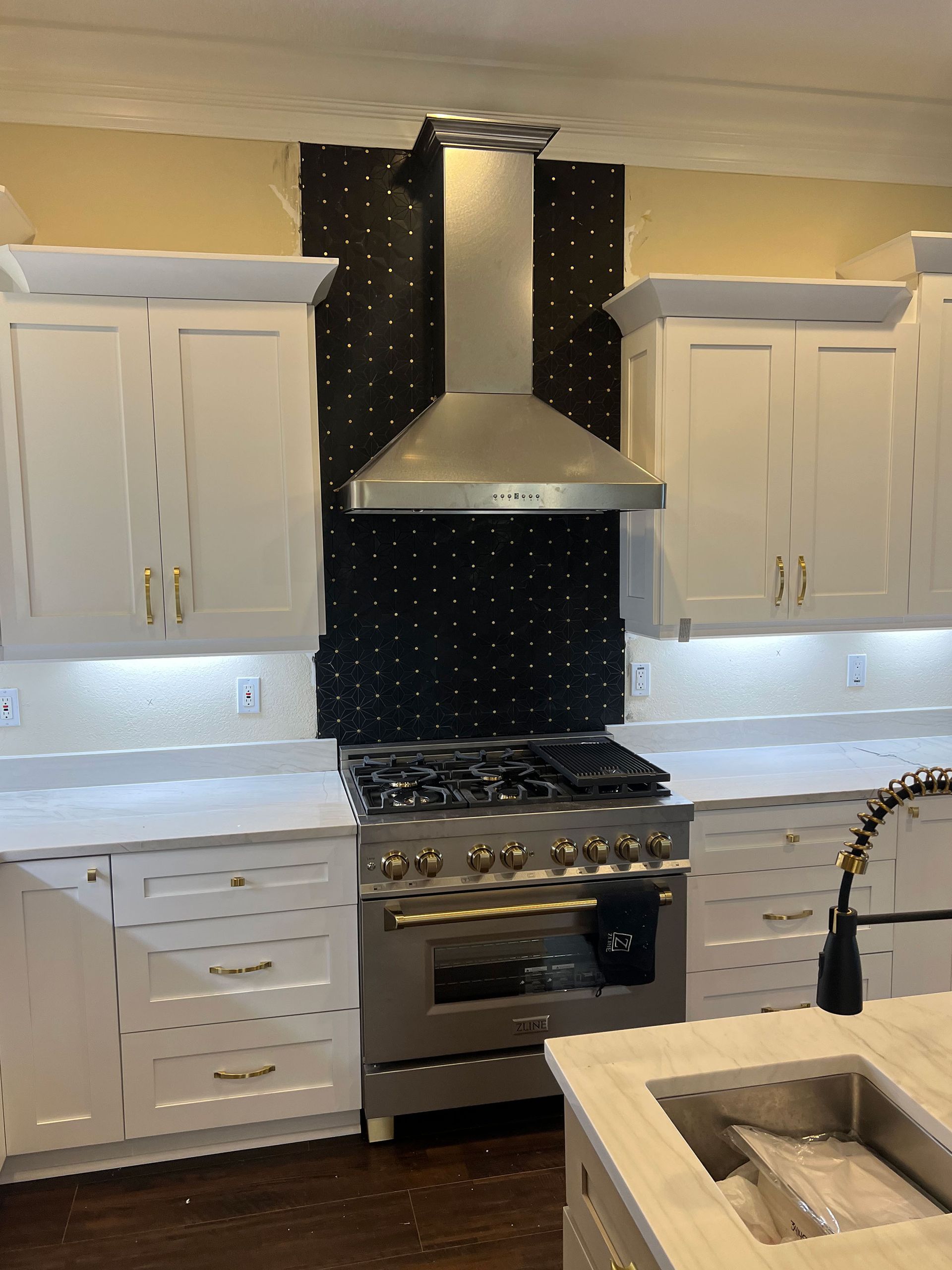 Modern kitchen with white cabinets, stainless steel range hood, gas stove, and black backsplash