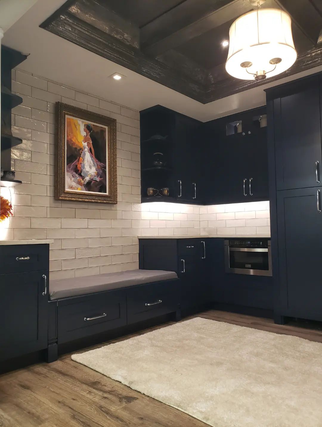 Modern kitchen with dark cabinets, white subway tile backsplash, framed wall art, and a ceiling light fixture