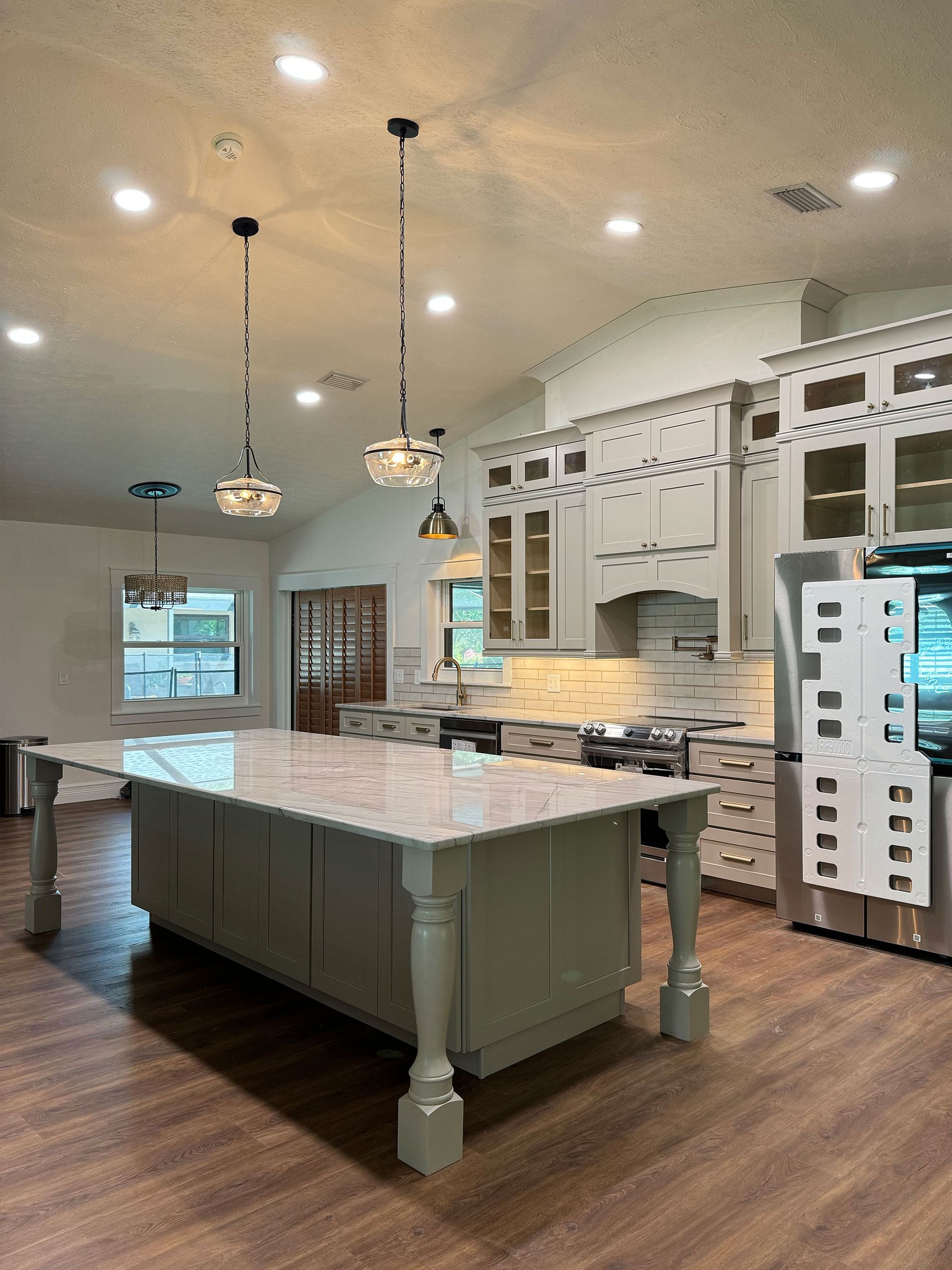 Bright kitchen with a large marble island, pendant lights, and white cabinets.
