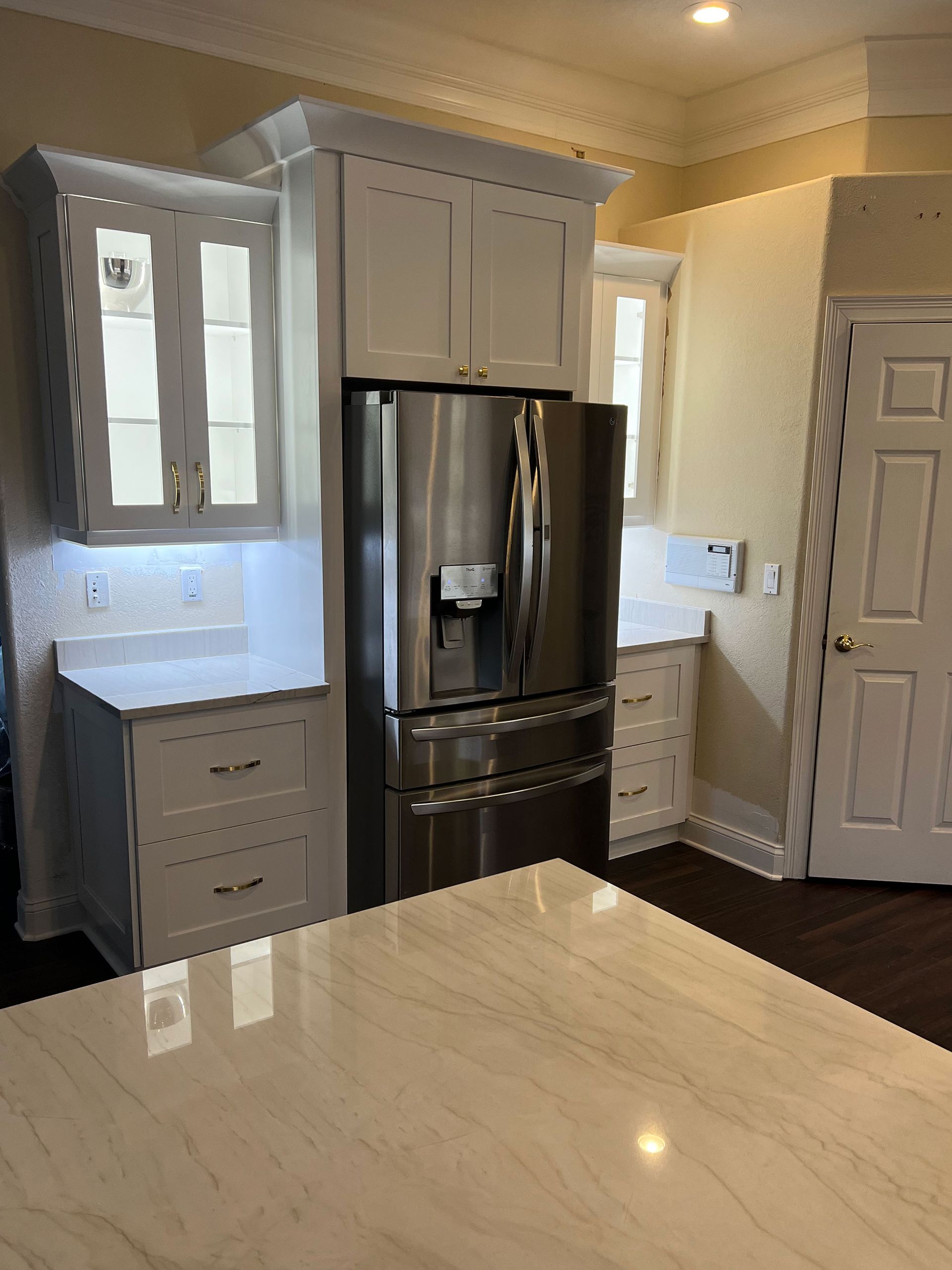 Bright modern kitchen with white cabinets, stainless steel fridge, and marble island countertop
