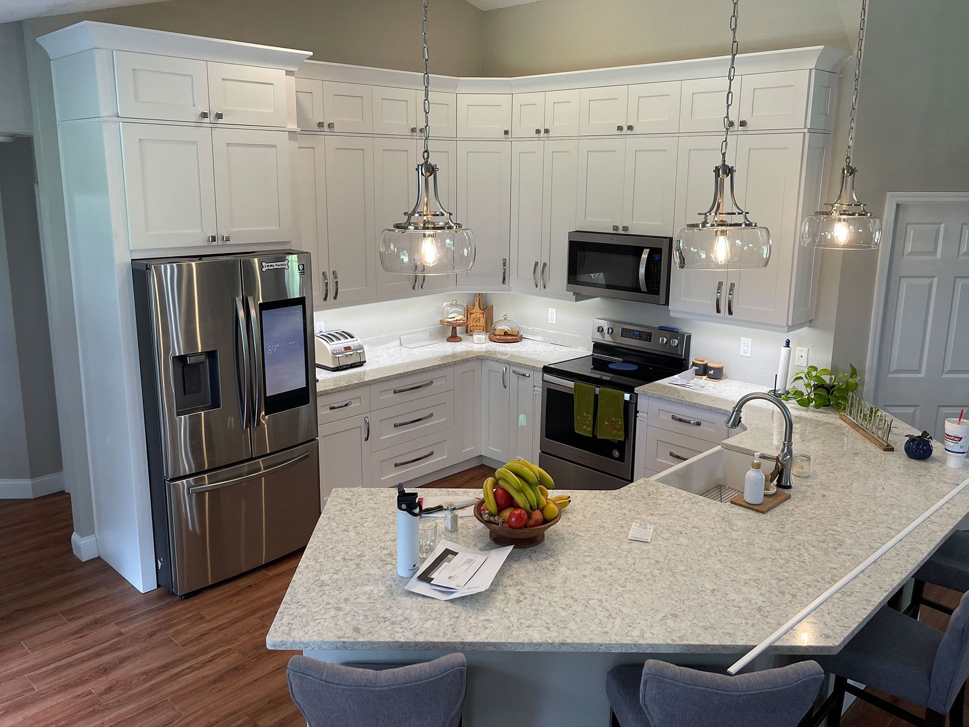 Bright modern kitchen with stainless steel appliances, white cabinets, and an island with fruit and a laptop.
