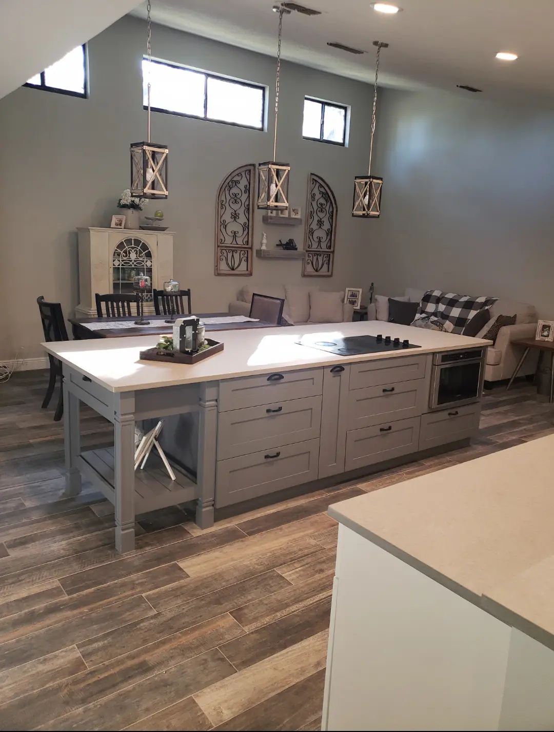 Modern kitchen with large white island, gray cabinets, wood floors, and wall art in a bright open room