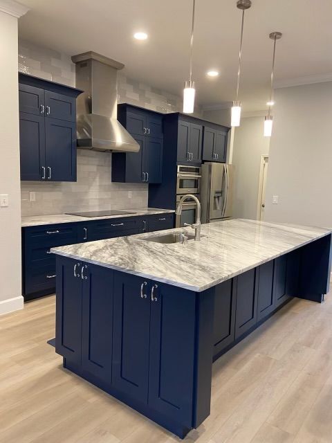 Modern kitchen with navy cabinets, marble island, stainless range hood, and pendant lights