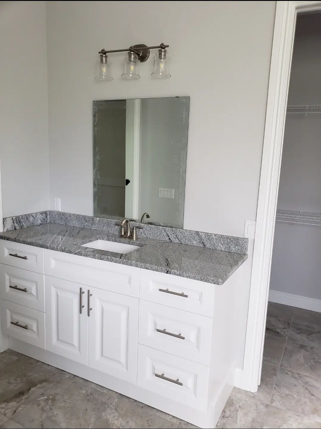 Bathroom vanity with white cabinets, speckled granite countertop, and mirror under a light fixture