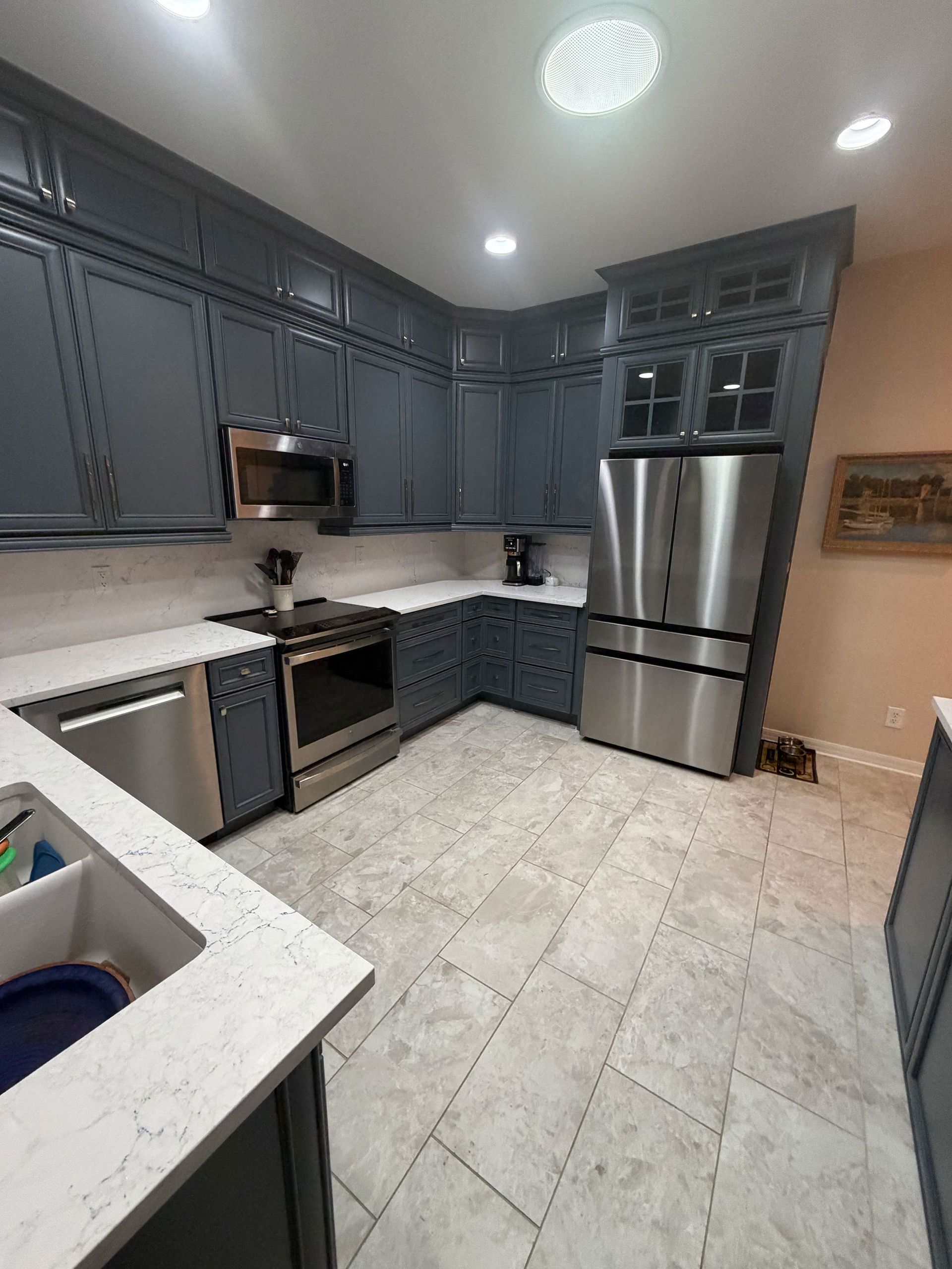 Modern gray kitchen with stainless steel appliances, white countertops, and tiled floor