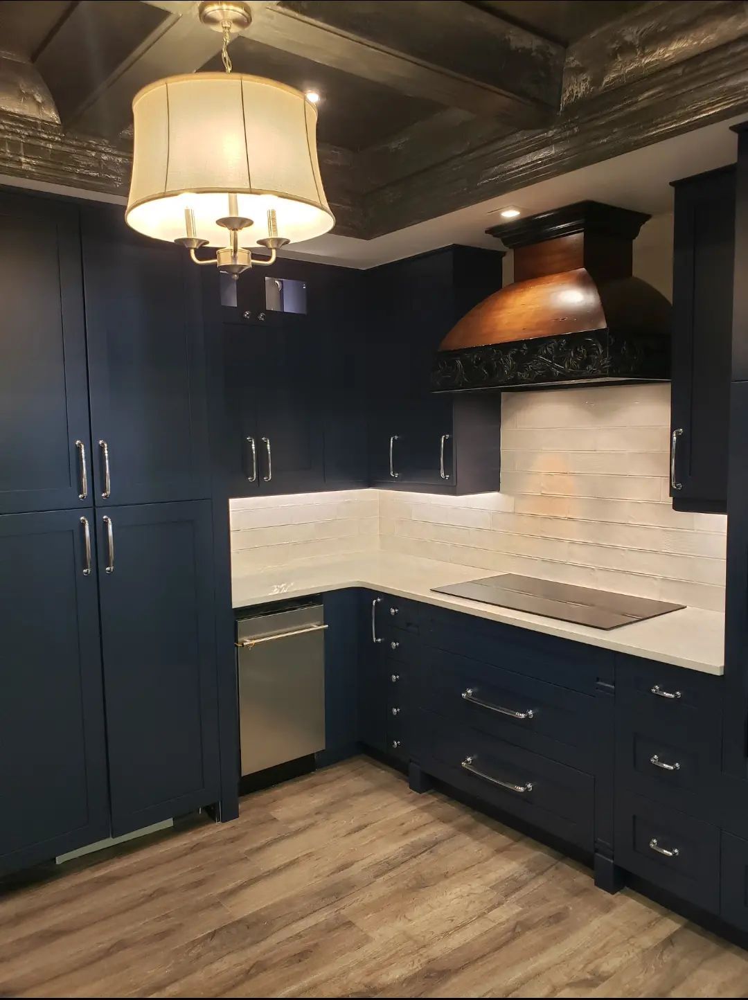 Dark navy kitchen with white tile backsplash, copper range hood, and a hanging light fixture.