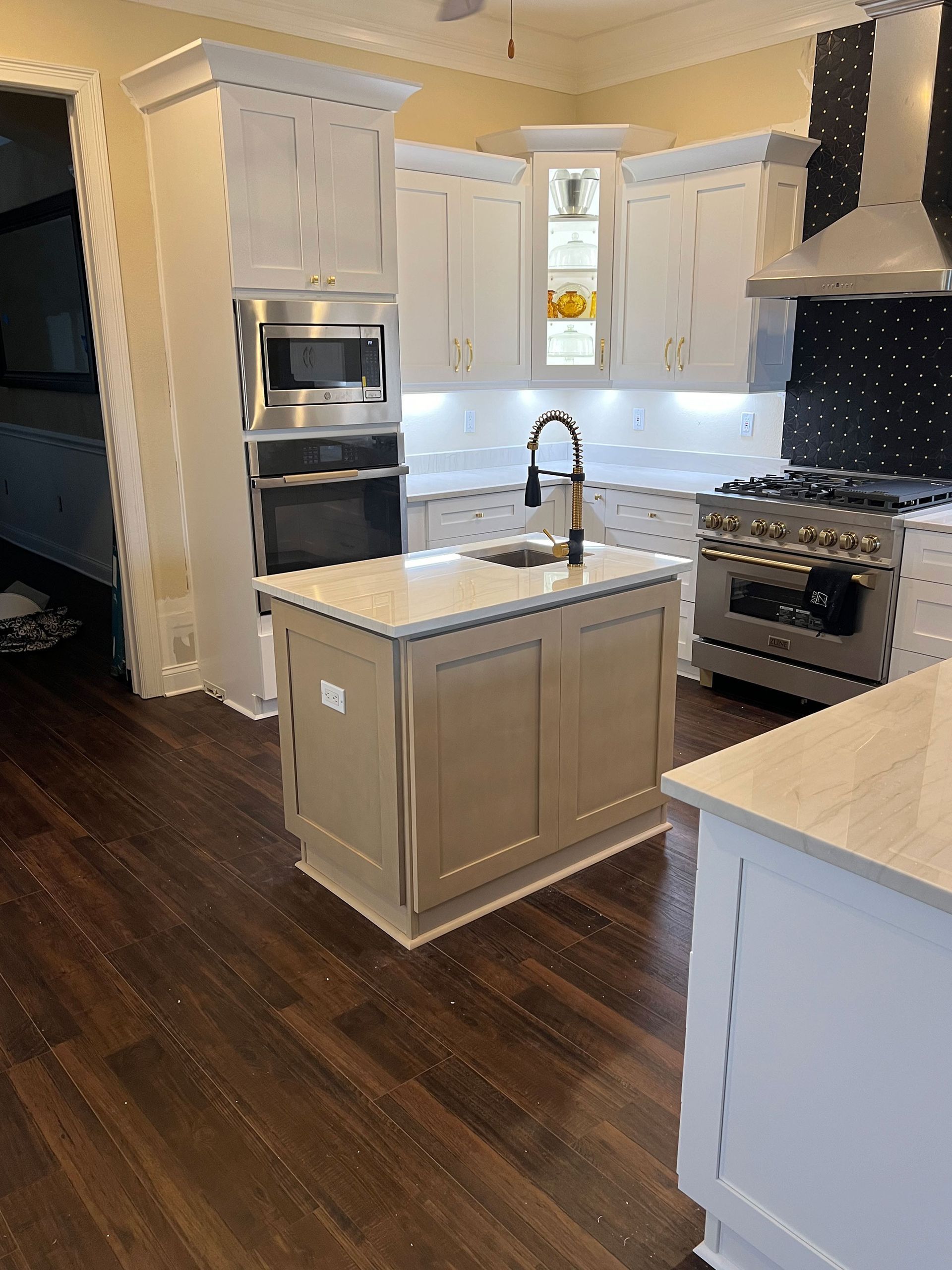 Bright modern kitchen with white cabinets, island sink, dark wood floors, and stainless steel stove and oven.