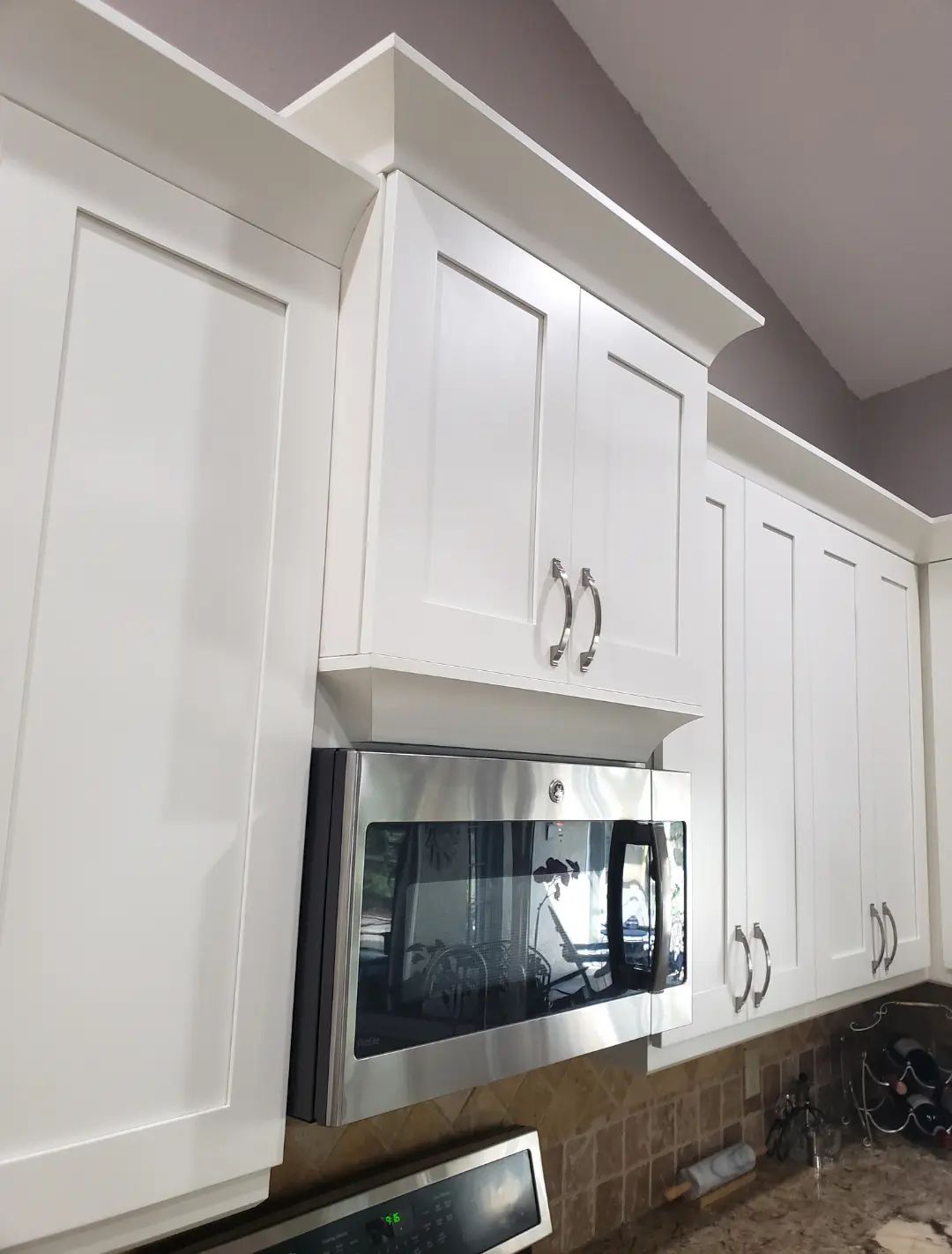 Kitchen with white cabinets and a stainless steel microwave above a tiled backsplash.