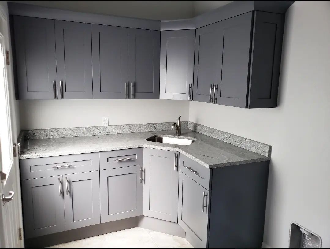Gray L-shaped kitchen cabinets with speckled countertop and corner sink against white walls