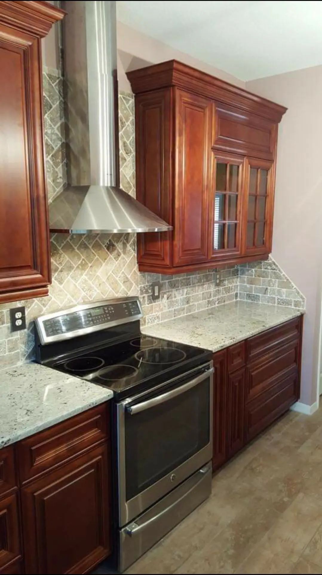 Modern kitchen with dark wood cabinets, stainless steel stove and hood, and light patterned backsplash
