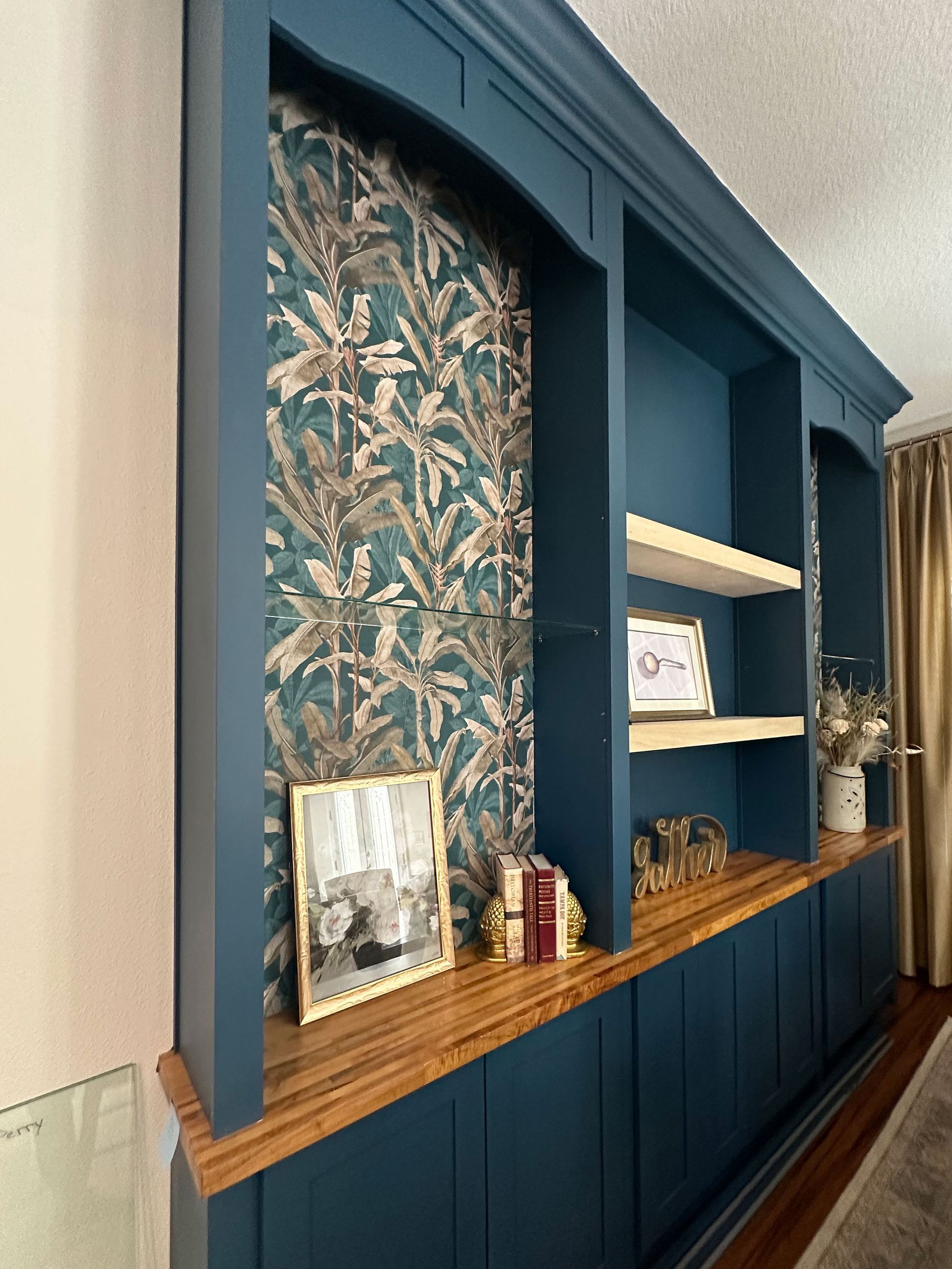 Built-in blue shelving with patterned wallpaper, wooden countertop, and framed decor in a hallway