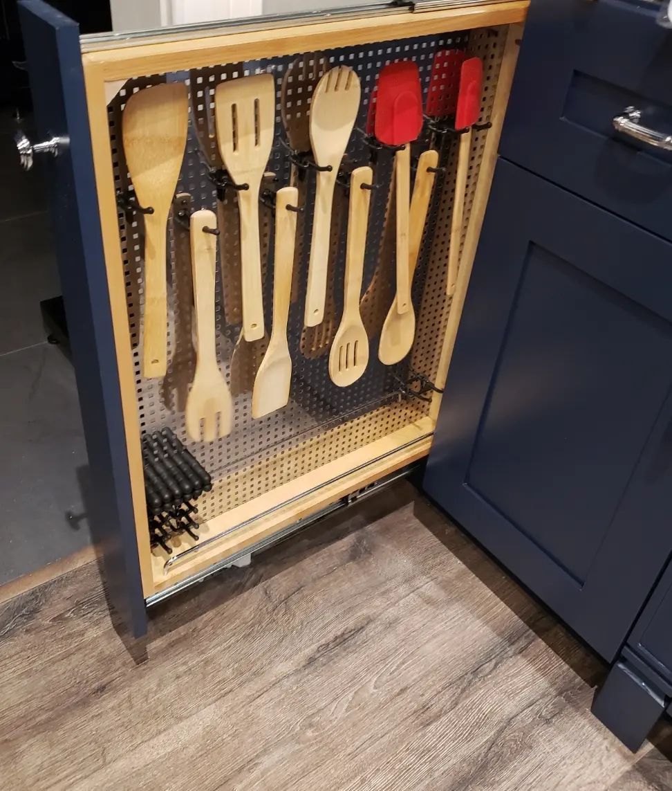 Kitchen cabinet drawer with hanging wooden and silicone cooking utensils on a pegboard organizer