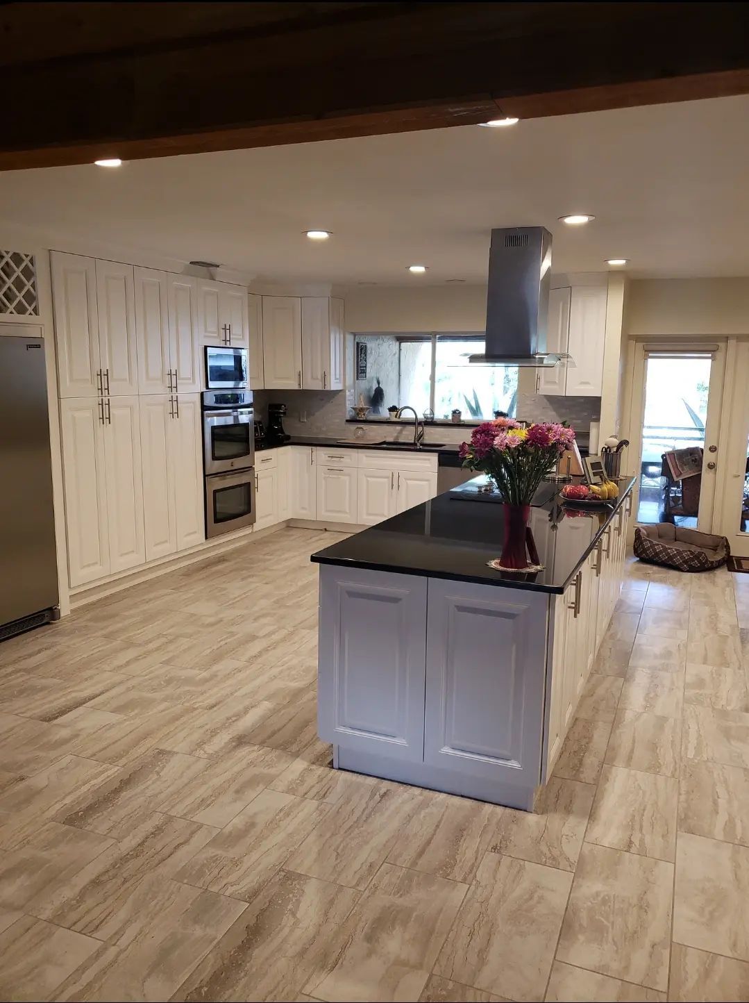 Modern open kitchen with light wood floors, gray island, black countertops, and pendant range hood