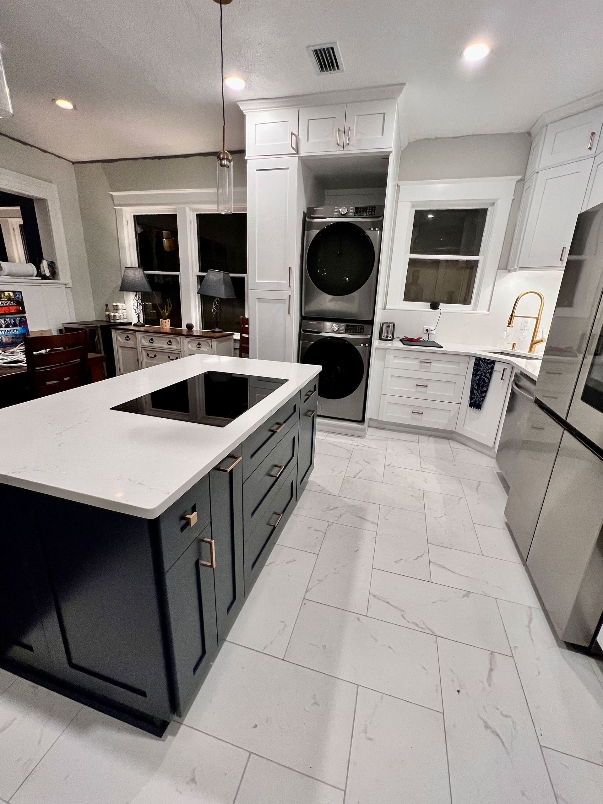 Modern white kitchen with dark island, built-in oven, and stacked washer-dryer at the back.