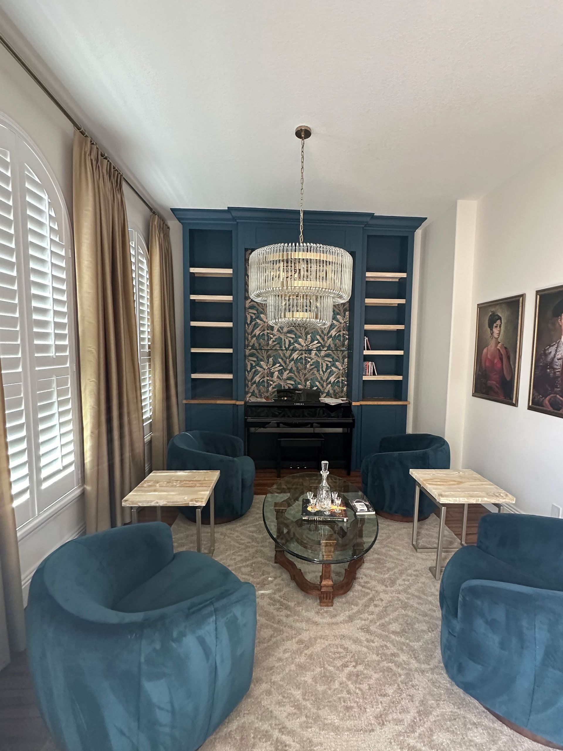 Blue living room with chandelier, fireplace, mirrored wall, and plush chairs on a patterned rug