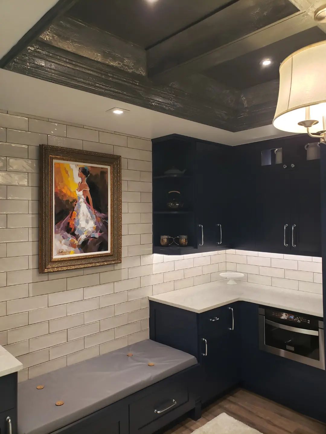 Cozy modern kitchen nook with navy cabinets, white tile backsplash, gray bench, and framed artwork