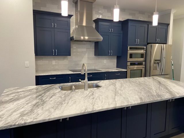 Modern kitchen with navy cabinets, marble island, stainless appliances, and light gray tile backsplash